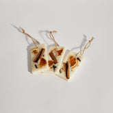 Boujie natural wax tag decoration with orange, cinnamon and clove, minimalist flat-lay on white surface for home scent styling.